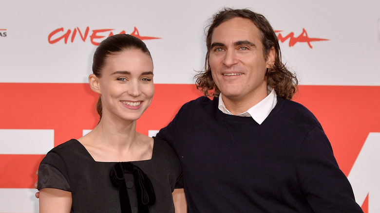 Rooney Mara indossa un abito nero con fiocco e Joaquin Phoenix indossa un maglione nero e una camicia bianca con colletto