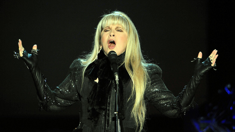 Stevie Nicks canta mentre indossa un cappotto di pelle nera abbagliante e guanti senza dita di pelle nera