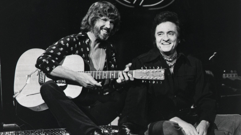 Kris Kristofferson e Johnny Cash sorridono insieme, Kristofferson con in mano una chitarra