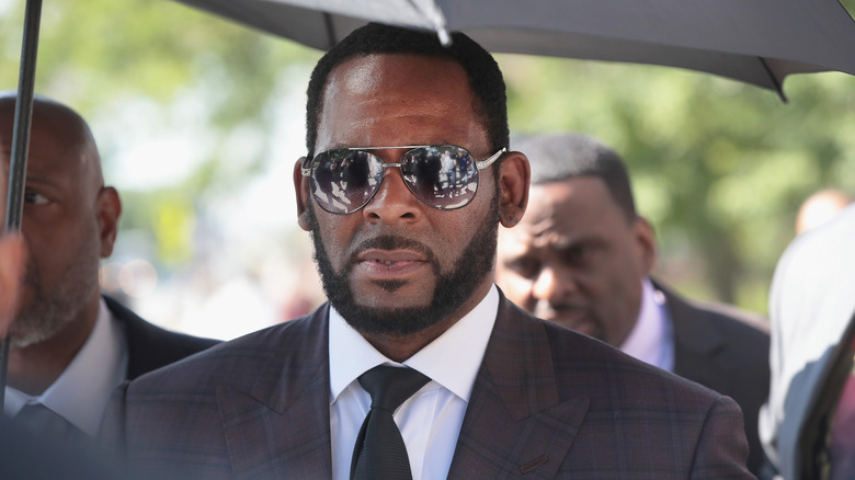 R. Kelly lascia un tribunale mentre indossa un abito sotto l'ombrello