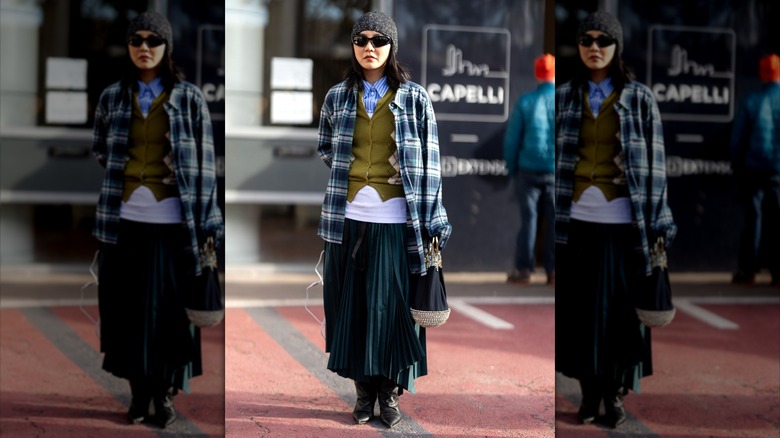 Donna con camicia a righe, maglione a rombi, giacca scozzese, maxi gonna plissettata