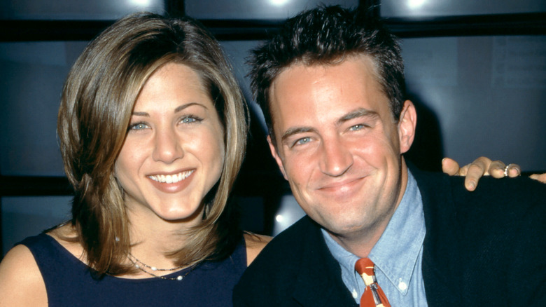 Jennifer Aniston in un abito blu e Matthew Perry in una giacca nera, camicia con colletto blu e cravatta colorata