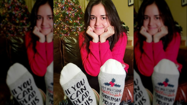 Danica McKellar posa per un selfie davanti al suo albero di Natale, indossando un maglione rosso e calzini natalizi.