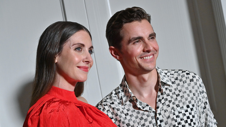 Alison Brie indossa un top rosso, Dave Franco sorride con una camicia a scacchi