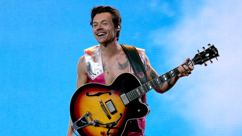 Harry Styles sul palco con in mano una chitarra e sorridente