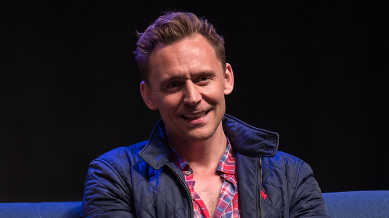 Tom Hiddleston sorridente mentre è seduto sul palco