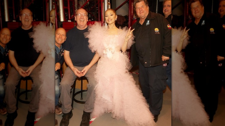 Ariana Grande posa nel backstage con i membri della troupe in un abito rosa a balze.