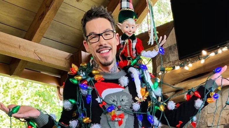 David Bromstad avvolto nelle luci di Natale con un elfo giocattolo sulla spalla