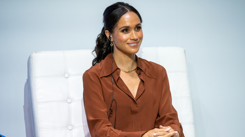 Meghan Markle vestita di marrone su una sedia bianca