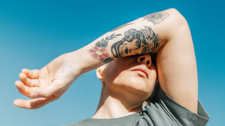 Persona che copre il viso con il braccio tatuato