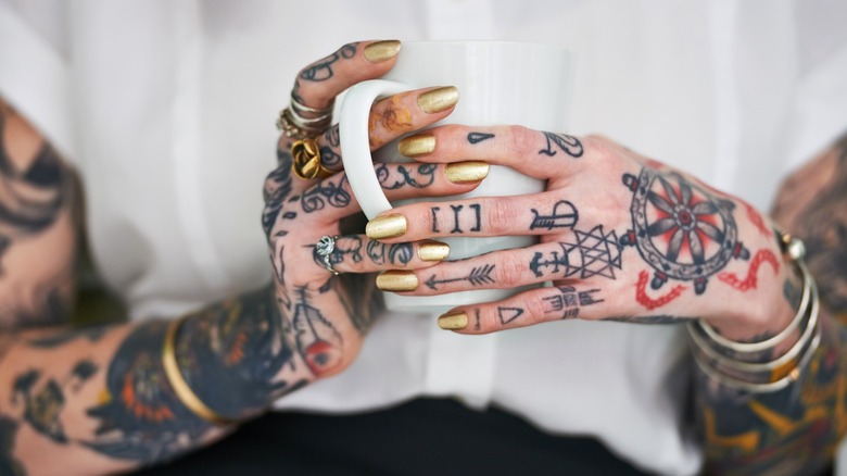 Le mani tatuate della donna che tengono la tazza